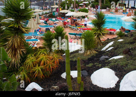 Holiday makers relaxing in the sun at a hotel pool beside a beautiful Cacti and Rock garden Stock Photo