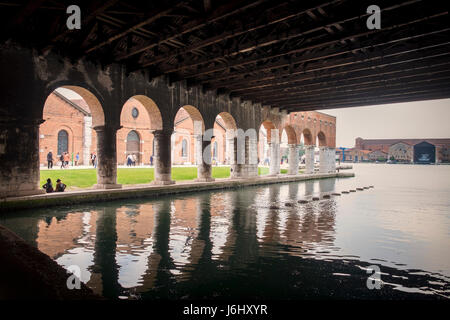 Venice, Castello, Arsenale harbour. View of old buildings from covered dock of Gaggiandre with people visiting the Venice Bienniale in the background Stock Photo