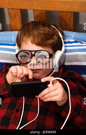 11-year old boy in bedroom using a smart phone to access the internet Stock Photo