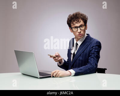 Funny businessman in glasses with laptop and phone, studio shot on gray background Stock Photo