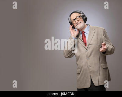 Portrait of senior man in headphones listening music, studio shot on gray background Stock Photo