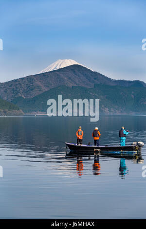 Three japanese men fishing in lake Ashinoko, with snow capped mount Fuji in the background. Stock Photo