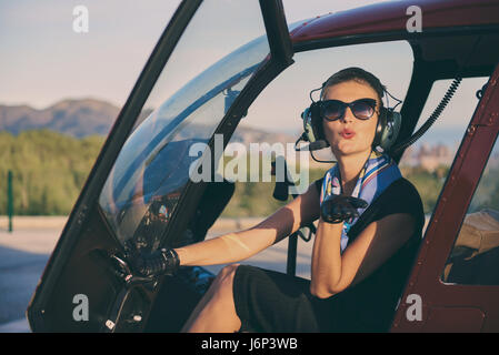 Attractive woman pilot sitting in the helicopter and blowing a kiss Stock Photo