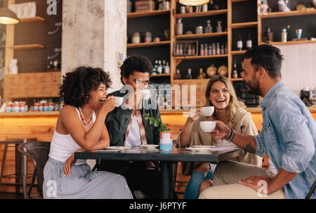 Diverse group of friends enjoying some coffee together in a restaurant and talking. Young people sitting around cafe table and drinking coffee. Stock Photo