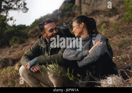 Young couple taking a break on a hike. Man and woman sitting and taking rest during hiking. Stock Photo