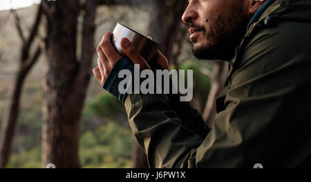 Close up shot of young male hiker drinking coffee. Cropped image of male hiker taking rest during hike. Stock Photo