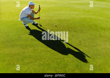 Pro golf player aiming shot with club on course. male golfer check line for putting golf ball on green grass. Stock Photo