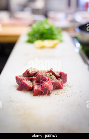 Chopped steak, seasoning, on a cutting board with produce in the background Stock Photo