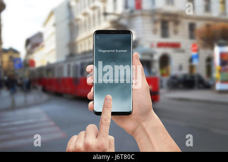 Fingerprint scanner security app on moder mobile phone. Man holding and touch round phone screen. Street in background. Stock Photo