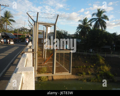 This photograph captures a sunset view over the San Miguel Bridge, located in the town of San Juan Poblacion, Bulacan, Philippines. The image highlights the natural beauty of the river and surrounding landscape during the golden hour. Stock Photo
