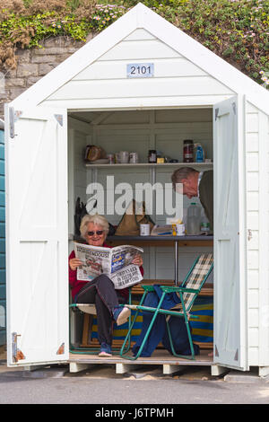 Bournemouth, Dorset, UK. 22nd May, 2017. UK weather: a warm and muggy start as visitors head to the beach early, as temperatures rise and forecasters are predicting the hottest day of the year so far this week. Mature couple at beach hut, woman sat reading Daily Mail newspaper.  Credit: Carolyn Jenkins/Alamy Live News Stock Photo