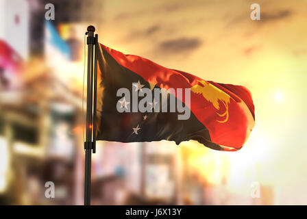 Papua New Guinea Flag Against City Blurred Background At Sunrise Backlight Stock Photo