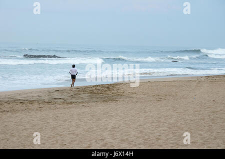 Lone male runner along Playa Bruja beach beside the waves of the Pacific Ocean on a cloudy day at RIU Emerald Bay Resort, Mazatlan, Sinaloa, Mexico. Stock Photo