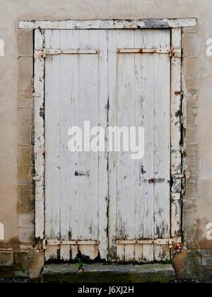 Old, white, wooden, double door with rotted edges. Rusty metal. Off white, stone building. Bayeux, Calvados, France. Stock Photo
