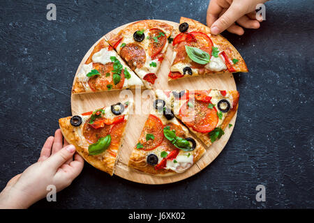 People Hands Taking Slices Of Italian Pizza. Italian Pizza and  Hands close up over black background. Stock Photo
