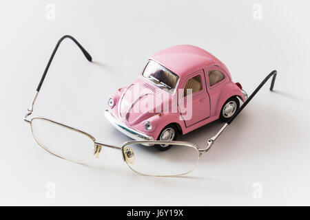 Pink toy car is on a white desk near the eyeglasses Stock Photo