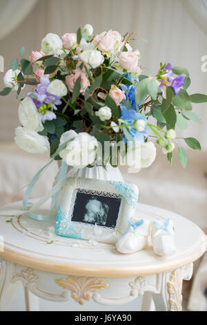 Children's shoes and ultrasound of the baby's fetus with a beautiful bouquet of flowers. Stock Photo