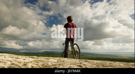 man on bicycle near a cliff with covered by forest hills Stock Photo