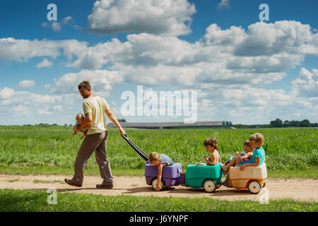 Father carrying baby son while pulling four children in a wagon Stock Photo