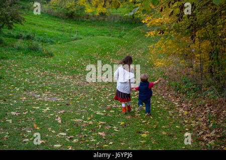 Two children holding hands running down a hill Stock Photo