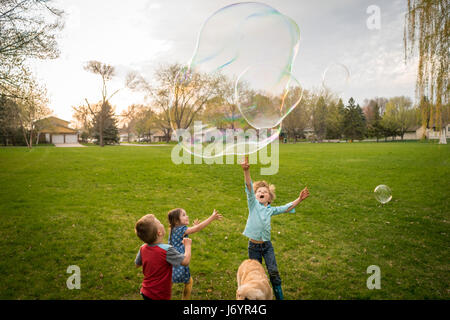 Three children playing with giant soap bubbles Stock Photo