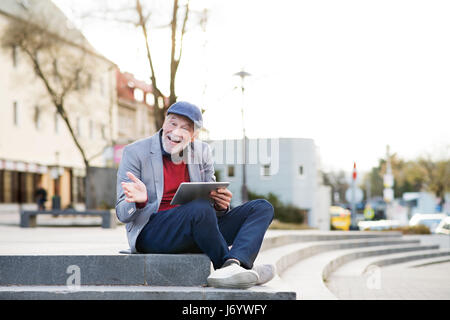 Handsome senior man with tablet in town sitting on stairs. Stock Photo