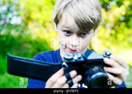 Sad boy looking at the open back of the camera and enlightened ruined film inside. Little child blond boy with an old camera shooting outdoor. Kid tak Stock Photo