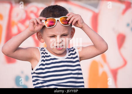 adorable little boy with white sunglasses and sailor stripes shirt on yellow and pink graffiti wall background Stock Photo