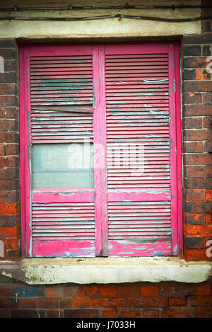 Faded and peeling red paint on shuttered window Stock Photo