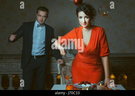 Woman in red dress threatens a fork, a man behind her is out of focus, in the hands of a knife. Stock Photo