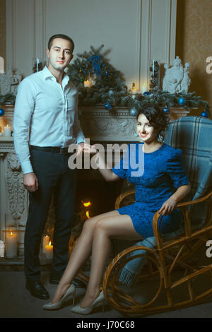 The man holding the hand of a woman who is sitting in a chair near the fireplace, in terms of burning candles. Stock Photo