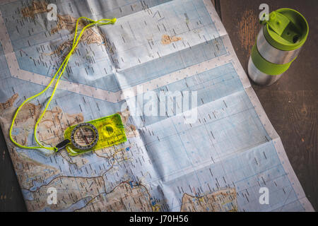 Fluorescent yellow compass lying on map of Lofoten islands, Norway on wooden table next to silver thermal mug Stock Photo