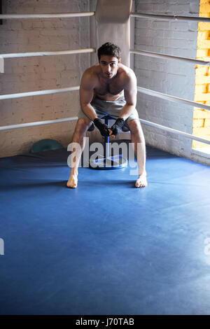 Young boxer sitting in the corner of boxing ring and looking camera Stock Photo