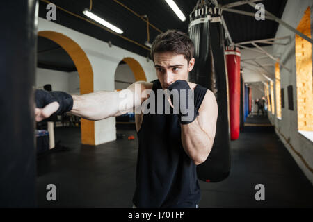 Concentrated boxer doing training in gym with punchbag Stock Photo