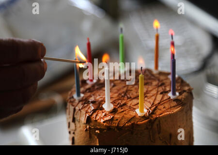 Lighting candles on chocolate birthday cake in office Stock Photo