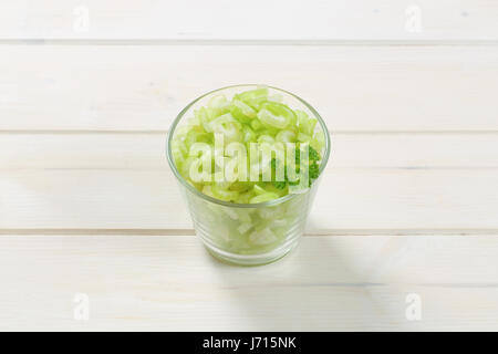 glass of chopped celery stems on white wooden background Stock Photo