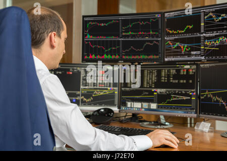 Rear view of stock trader analyzing data at multiple computer screens. Stock Photo