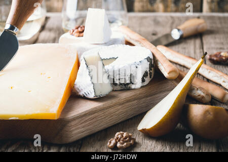 Cheese platter served with white wine, jam and walnuts on wooden board on rustic table Stock Photo