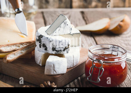 Cheese platter served with white wine, jam and walnuts on wooden board on rustic table Stock Photo