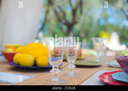 Dining set on outdoor table, focus on glasses, relax and tranquil feeling with lemon fruits in plate in background Stock Photo