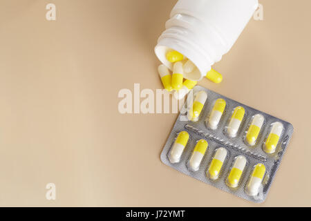 Yellow medicine capsules. Pills blister pack and tablets bottle on beige background Stock Photo