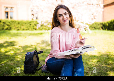 against background of green meadow sat young, charming girl - student reads book Stock Photo