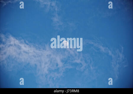 moon in daytime blue sky cirrus clouds white and stringy Stock Photo