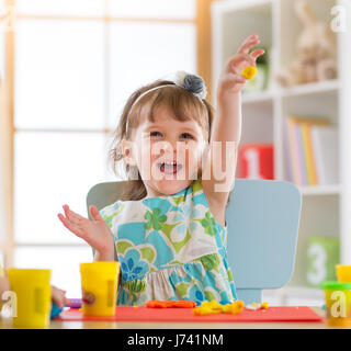 Smiling little girl is learning to use colorful play dough in a well lit room near window Stock Photo