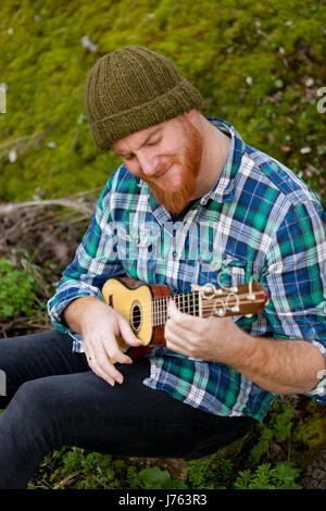 Hipster man with red beard playing a ukulele in the field Stock Photo