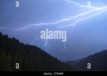 A horizontal cloud-to-cloud lightning in a heavy thunderstorm at night over a mountainous forest in Austria. Stock Photo