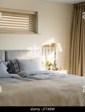Striped duvet and cushion covers on bed with patterned headboard Stock Photo