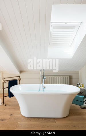 Free standing bath in top floor master bedroom with pitched ceiling and shutters. Stock Photo