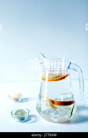 Citrus fruits slices with water in jug on table against wall Stock Photo
