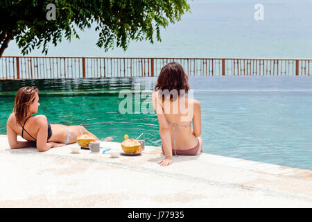 Female friends relaxing at poolside Stock Photo